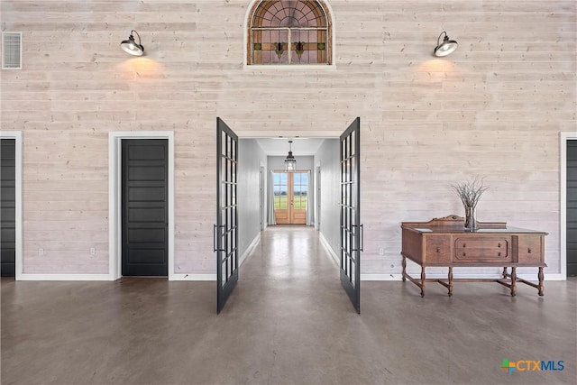 hall featuring a high ceiling, concrete flooring, and french doors