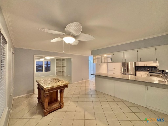 kitchen with ornamental molding, stainless steel fridge, light tile patterned floors, and white cabinets