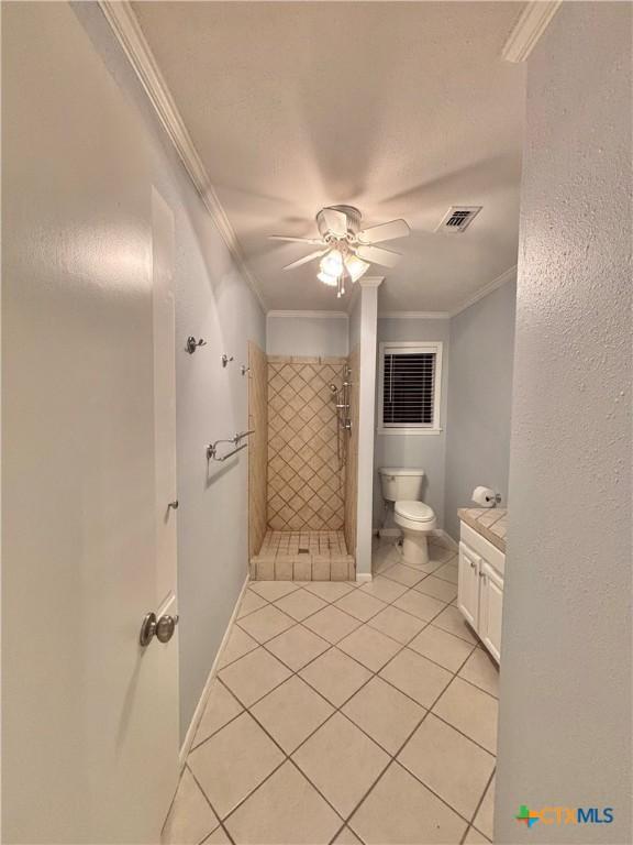 bathroom featuring ceiling fan, tile patterned flooring, vanity, a tile shower, and ornamental molding