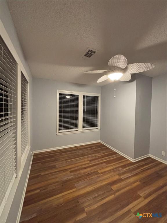 empty room with ceiling fan, dark wood-type flooring, and a textured ceiling