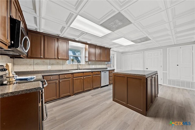 kitchen with sink, appliances with stainless steel finishes, tasteful backsplash, a kitchen island, and light wood-type flooring