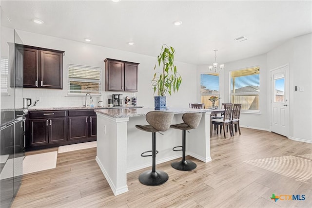 kitchen featuring light wood finished floors, a kitchen island, light stone counters, a breakfast bar, and decorative light fixtures