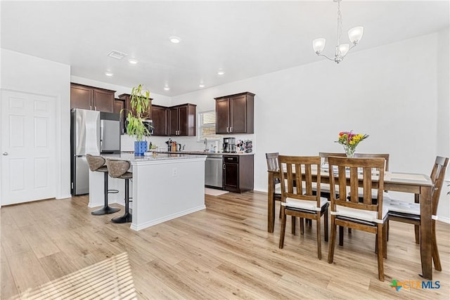 kitchen with light wood finished floors, hanging light fixtures, appliances with stainless steel finishes, dark brown cabinetry, and a kitchen island