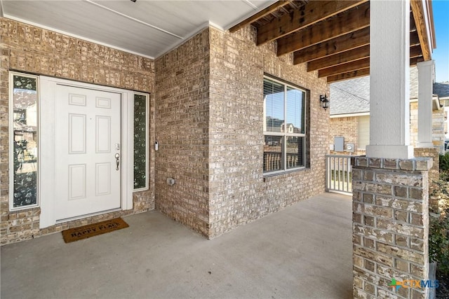 entrance to property featuring a porch and brick siding