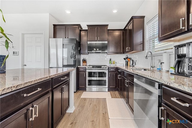 kitchen featuring light stone counters, appliances with stainless steel finishes, a sink, dark brown cabinetry, and light wood-type flooring