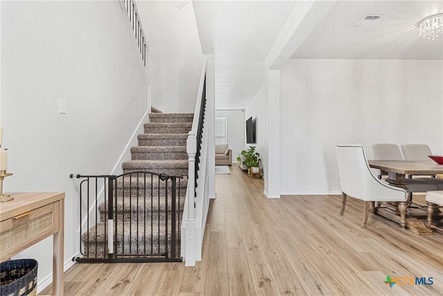 stairs featuring an inviting chandelier, baseboards, visible vents, and wood finished floors