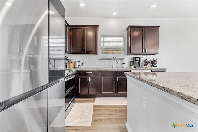 kitchen with stainless steel appliances, dark brown cabinetry, decorative backsplash, and light stone countertops