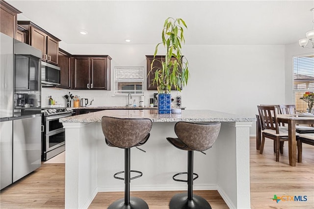 kitchen featuring light wood finished floors, appliances with stainless steel finishes, light stone counters, and a center island