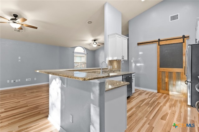 kitchen with stone counters, stainless steel appliances, white cabinets, a barn door, and kitchen peninsula