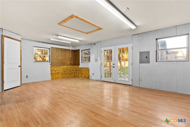 unfurnished living room featuring plenty of natural light, electric panel, light wood-type flooring, and french doors