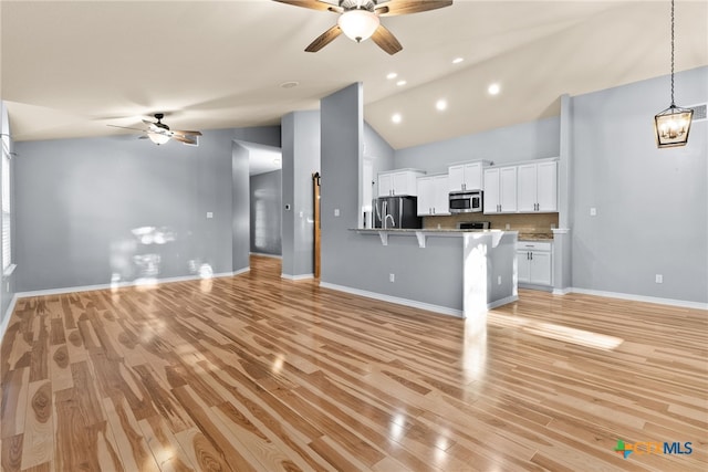 kitchen with light hardwood / wood-style flooring, appliances with stainless steel finishes, ceiling fan with notable chandelier, decorative backsplash, and white cabinets