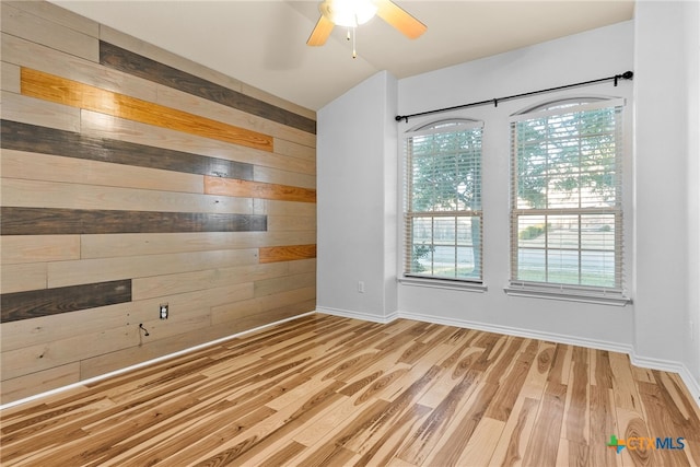 empty room featuring ceiling fan, wooden walls, and light wood-type flooring