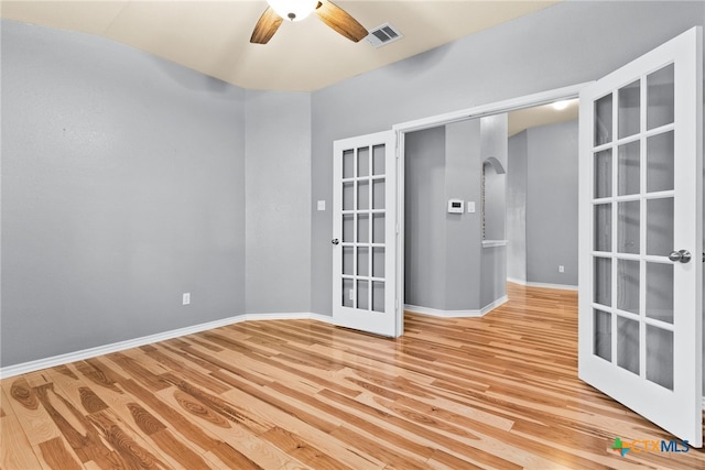 empty room with french doors, ceiling fan, and light wood-type flooring