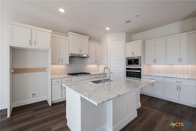 kitchen featuring a center island with sink, oven, sink, built in microwave, and white cabinetry