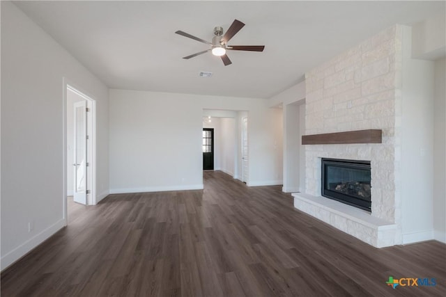 unfurnished living room with a stone fireplace, ceiling fan, and dark wood-type flooring