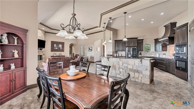 tiled dining space featuring a towering ceiling, crown molding, a fireplace, a raised ceiling, and a chandelier