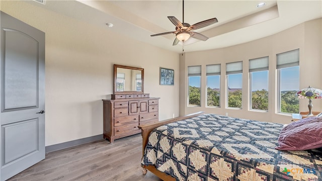 bedroom with ceiling fan, multiple windows, a raised ceiling, and light hardwood / wood-style flooring