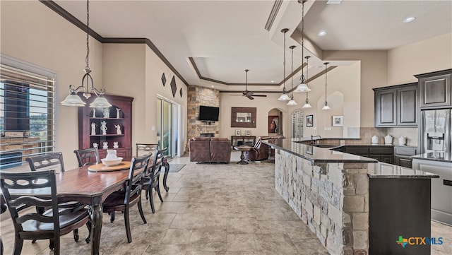 dining area featuring a stone fireplace, a towering ceiling, ornamental molding, and ceiling fan