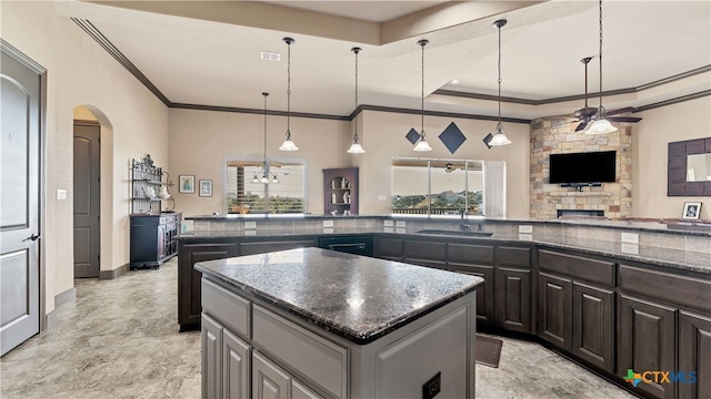 kitchen featuring a fireplace, crown molding, hanging light fixtures, sink, and a center island