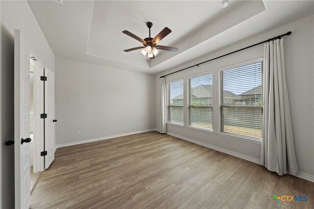 unfurnished room featuring light wood-style floors, baseboards, a tray ceiling, and a ceiling fan