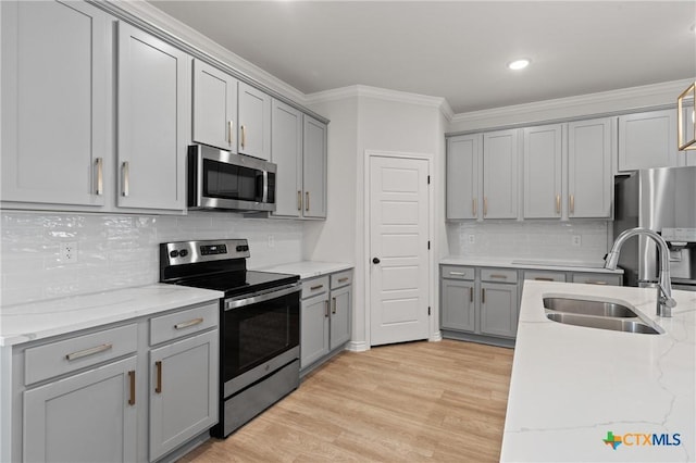 kitchen with a sink, appliances with stainless steel finishes, gray cabinets, and crown molding