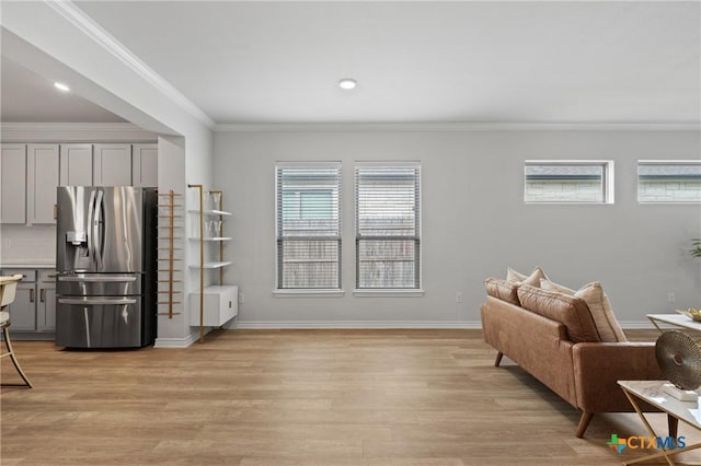 living area with baseboards, ornamental molding, and light wood-style floors