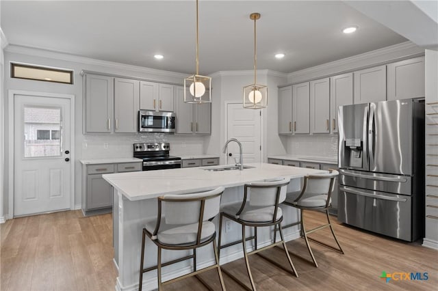 kitchen featuring light wood-style flooring, stainless steel appliances, a sink, ornamental molding, and gray cabinets