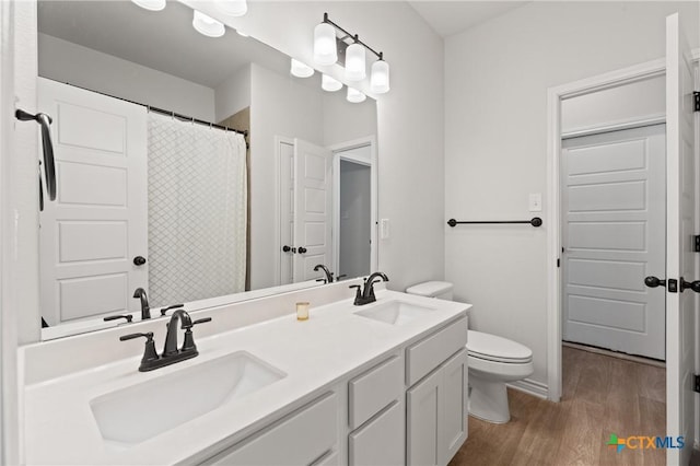 full bath with toilet, double vanity, a sink, and wood finished floors