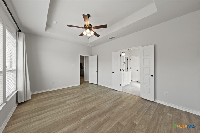 unfurnished bedroom with a ceiling fan, visible vents, baseboards, light wood finished floors, and a raised ceiling