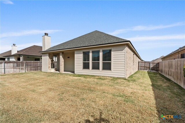 rear view of house with a shingled roof, a lawn, a fenced backyard, and brick siding