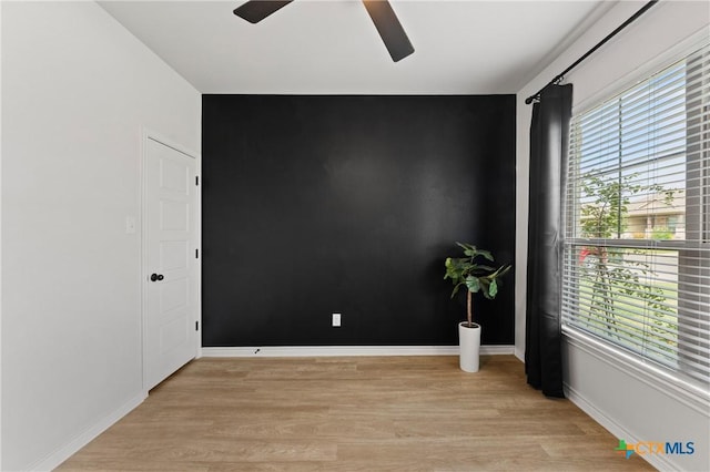 empty room featuring light wood finished floors, ceiling fan, an accent wall, and baseboards