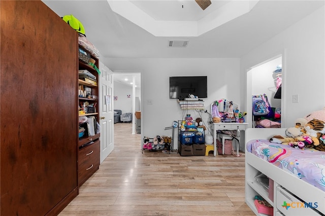 bedroom featuring light wood-type flooring, a tray ceiling, and ceiling fan