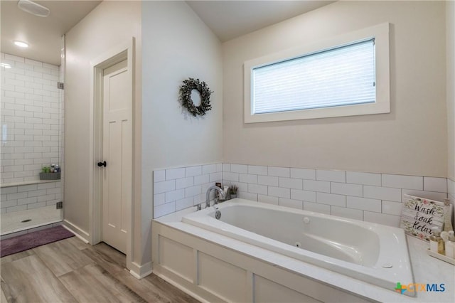 full bath featuring a stall shower, a garden tub, and wood finished floors