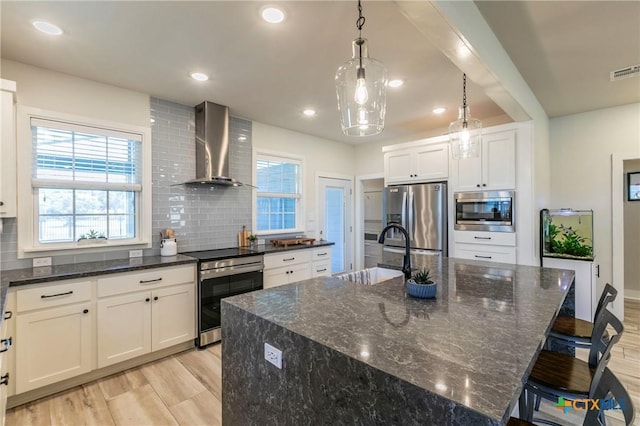 kitchen with wall chimney range hood, light wood-style flooring, stainless steel appliances, and a sink