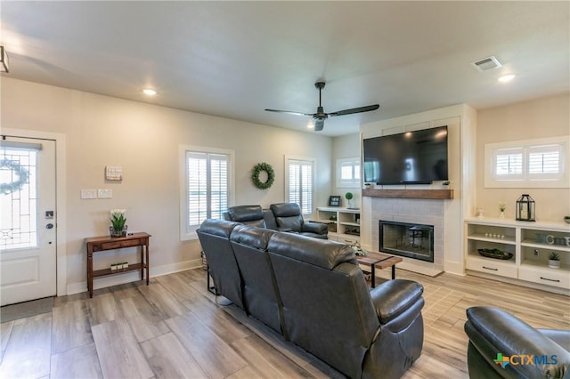 living area featuring a fireplace, a ceiling fan, visible vents, baseboards, and light wood finished floors