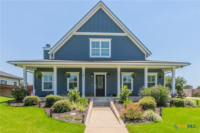 view of front facade with board and batten siding, covered porch, fence, and a front lawn