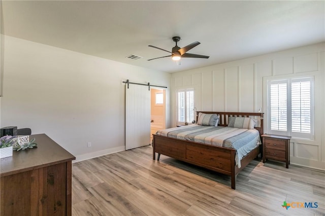 bedroom featuring light wood-style floors, multiple windows, a decorative wall, and a barn door