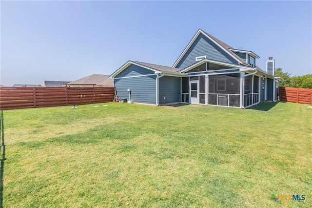 back of house with a sunroom, a fenced backyard, a chimney, and a yard