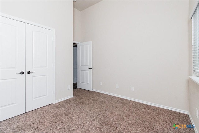 unfurnished bedroom with a closet, carpet floors, and a towering ceiling