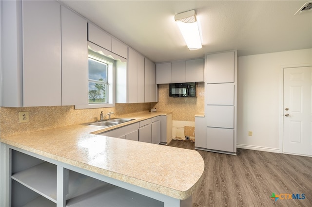 kitchen featuring sink, light wood-type flooring, kitchen peninsula, and tasteful backsplash