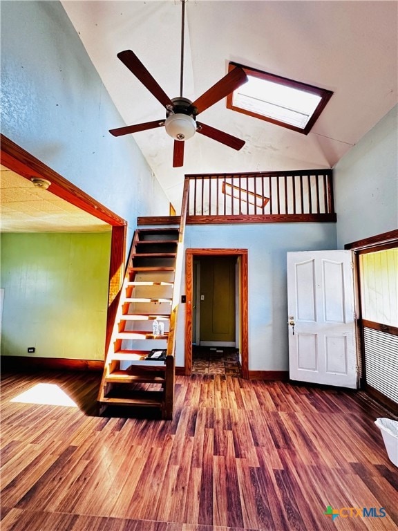 stairs featuring ceiling fan, wood-type flooring, a skylight, and high vaulted ceiling