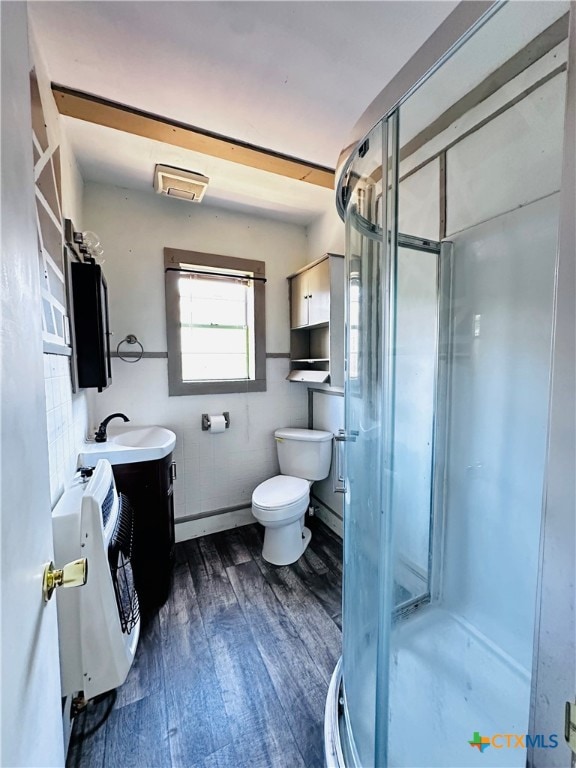 bathroom featuring toilet, hardwood / wood-style flooring, heating unit, an enclosed shower, and vanity