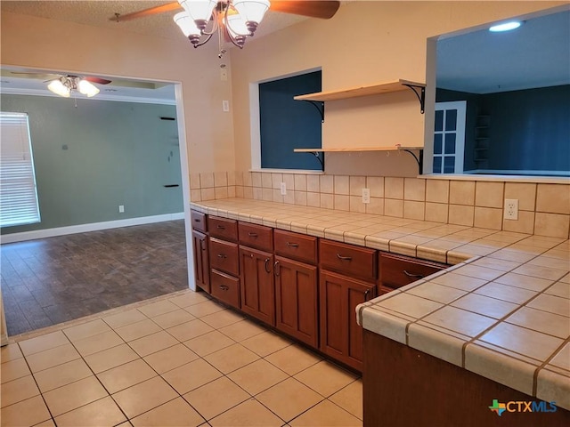 kitchen with an inviting chandelier, backsplash, tile countertops, light hardwood / wood-style floors, and a textured ceiling