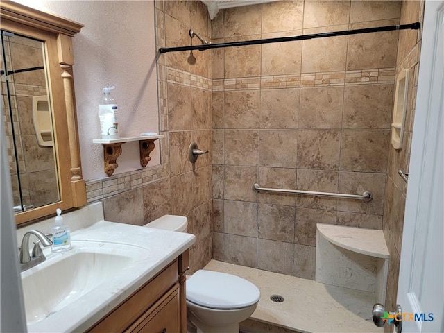 bathroom with a tile shower, vanity, and toilet