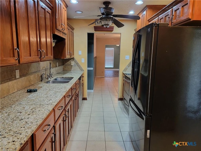 kitchen with light stone countertops, sink, ceiling fan, black fridge, and light tile patterned floors