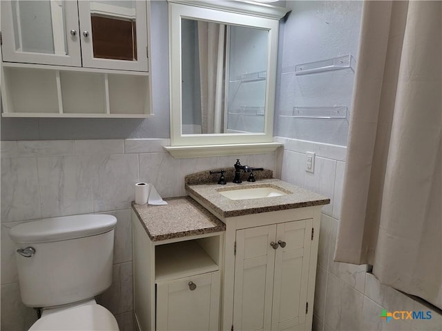 bathroom with vanity, toilet, and tile walls