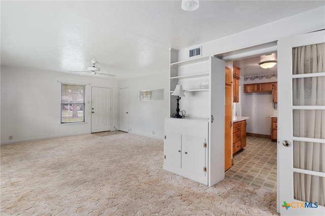 interior space with a textured ceiling, light colored carpet, and ceiling fan