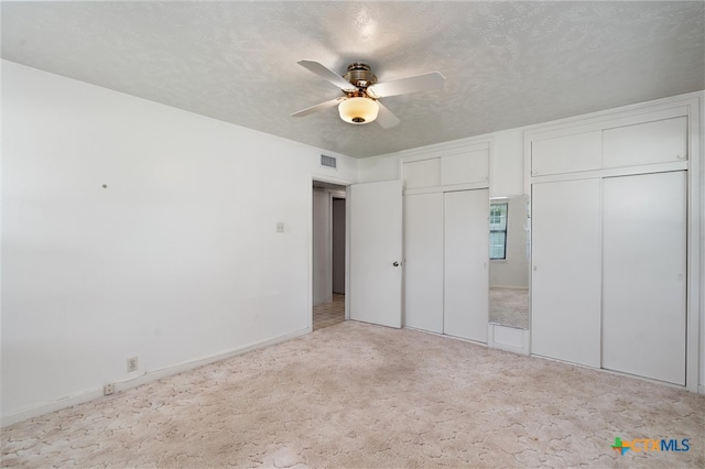 unfurnished bedroom with light colored carpet, a textured ceiling, two closets, and ceiling fan