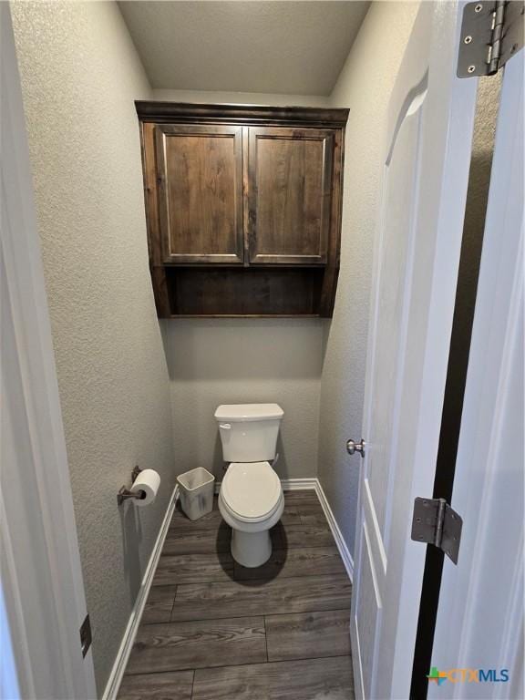 bathroom with toilet, wood finished floors, baseboards, and a textured wall