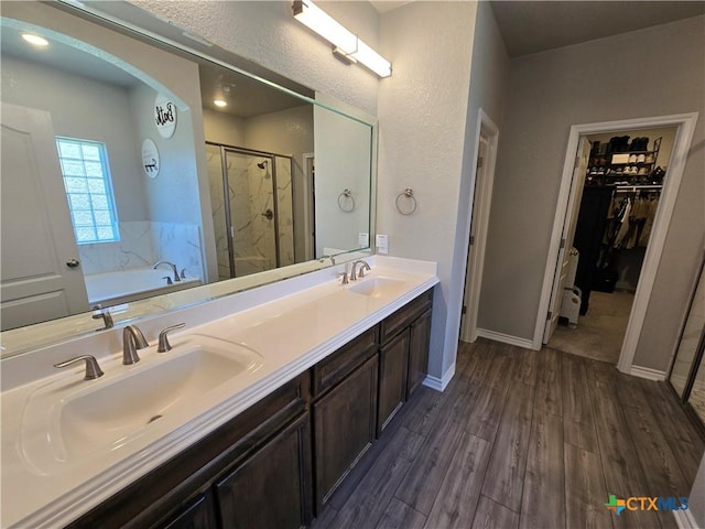bathroom featuring wood finished floors, a bath, a spacious closet, a shower stall, and a sink
